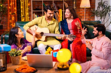 Diwali kutlamaları sırasında şarkı söyleyen arkadaşlar, Hint Asyalı genç evli çift geleneksel şenlik kıyafetleriyle gitar ve müzik eşliğinde ev sahipliği yapıyor dekore edilmiş evlerde Deepavali gecesinin tadını çıkarıyorlar.