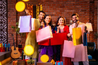 Gösterişli Diwali alışveriş torbaları ve tebessümlerle selamlaşan Hintli Asyalı genç evli çiftler dekore edilmiş evlerin iç kısımlarında geleneksel şenlik kıyafetleri içinde ve kameraya neşe dolu alışveriş torbaları gösteriyorlar.