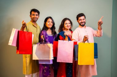 Gösterişli Diwali alışveriş torbaları ve tebessümlerle selamlaşan Hintli Asyalı genç evli çiftler dekore edilmiş evlerin iç kısımlarında geleneksel şenlik kıyafetleri içinde ve kameraya neşe dolu alışveriş torbaları gösteriyorlar.