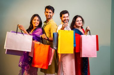 Gösterişli Diwali alışveriş torbaları ve tebessümlerle selamlaşan Hintli Asyalı genç evli çiftler dekore edilmiş evlerin iç kısımlarında geleneksel şenlik kıyafetleri içinde ve kameraya neşe dolu alışveriş torbaları gösteriyorlar.