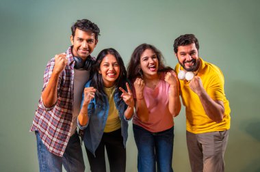 Üniversite öğrencileri zaferlerini kutluyorlar, Hintli üniversite gençleri yeşil duvara karşı ayakta duruyorlar, gülümsüyorlar, tezahürat yapıyorlar, akademik başarı üstüne sevinçle yumruklarını kaldırıyorlar.