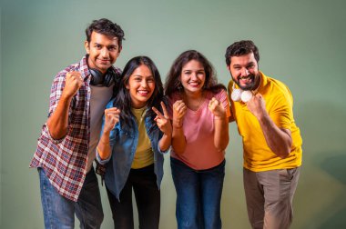 Üniversite öğrencileri zaferlerini kutluyorlar, Hintli üniversite gençleri yeşil duvara karşı ayakta duruyorlar, gülümsüyorlar, tezahürat yapıyorlar, akademik başarı üstüne sevinçle yumruklarını kaldırıyorlar.