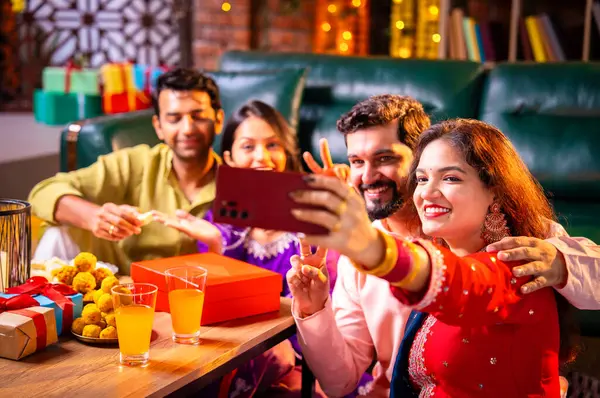 Arkadaşlarıyla Diwali selfie çeken Hindu genç evli çift Hindu festivali Deepavali 'yi kutlamak için dekore edilmiş evde laddu barfi şekerlerini tıklayarak selfie çekiyor.