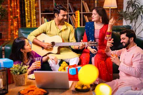Diwali kutlamaları sırasında şarkı söyleyen arkadaşlar, Hint Asyalı genç evli çift geleneksel şenlik kıyafetleriyle gitar ve müzik eşliğinde ev sahipliği yapıyor dekore edilmiş evlerde Deepavali gecesinin tadını çıkarıyorlar.