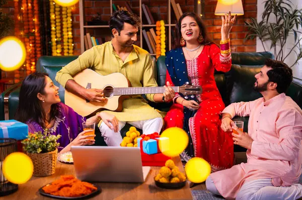 Diwali kutlamaları sırasında şarkı söyleyen arkadaşlar, Hint Asyalı genç evli çift geleneksel şenlik kıyafetleriyle gitar ve müzik eşliğinde ev sahipliği yapıyor dekore edilmiş evlerde Deepavali gecesinin tadını çıkarıyorlar.