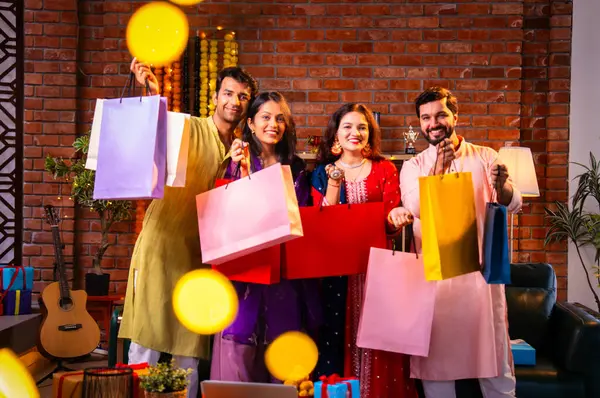 Gösterişli Diwali alışveriş torbaları ve tebessümlerle selamlaşan Hintli Asyalı genç evli çiftler dekore edilmiş evlerin iç kısımlarında geleneksel şenlik kıyafetleri içinde ve kameraya neşe dolu alışveriş torbaları gösteriyorlar.