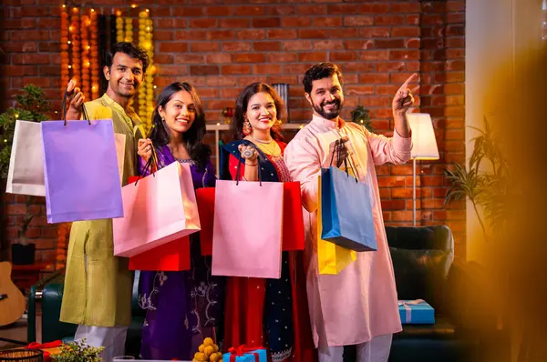 Gösterişli Diwali alışveriş torbaları ve tebessümlerle selamlaşan Hintli Asyalı genç evli çiftler dekore edilmiş evlerin iç kısımlarında geleneksel şenlik kıyafetleri içinde ve kameraya neşe dolu alışveriş torbaları gösteriyorlar.