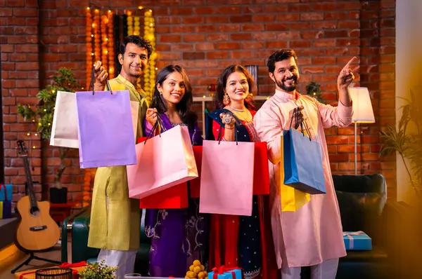 Gösterişli Diwali alışveriş torbaları ve tebessümlerle selamlaşan Hintli Asyalı genç evli çiftler dekore edilmiş evlerin iç kısımlarında geleneksel şenlik kıyafetleri içinde ve kameraya neşe dolu alışveriş torbaları gösteriyorlar.