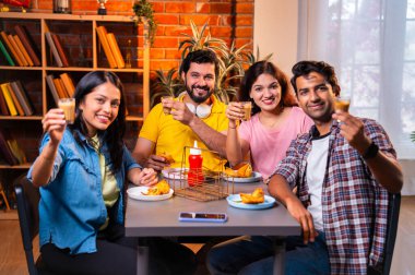 Hintli arkadaşlar sıcak çayın keyfini çıkarıyorlar, Asyalı genç üniversite öğrencileri kapalı bir lokantada oturmuş çay içiyor ya da cam bardaklardan kahve içiyor, arkadaşça sohbetler sırasında gülümsüyor ve kaynaşıyorlar.