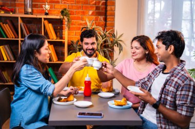 Hintli arkadaşlar sıcak çayın keyfini çıkarıyorlar, Asyalı genç üniversite öğrencileri kapalı bir lokantada oturmuş çay içiyor ya da cam bardaklardan kahve içiyor, arkadaşça sohbetler sırasında gülümsüyor ve kaynaşıyorlar.