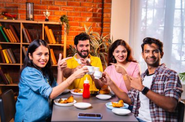 Hintli arkadaşlar sıcak çayın keyfini çıkarıyorlar, Asyalı genç üniversite öğrencileri kapalı bir lokantada oturmuş çay içiyor ya da cam bardaklardan kahve içiyor, arkadaşça sohbetler sırasında gülümsüyor ve kaynaşıyorlar.