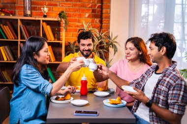 Hintli arkadaşlar sıcak çayın keyfini çıkarıyorlar, Asyalı genç üniversite öğrencileri kapalı bir lokantada oturmuş çay içiyor ya da cam bardaklardan kahve içiyor, arkadaşça sohbetler sırasında gülümsüyor ve kaynaşıyorlar.