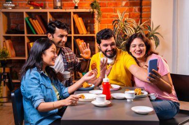 Samosa ve chai içerisindeyken arkadaşlarıyla video görüşmelerine katılan, Kafe 'de gülümseyen, akıllı telefonlarla sohbet eden, kapalı alanda neşeli anları paylaşan, arkadaşlarıyla iletişim kuran Hintli Asyalı üniversite arkadaşları.