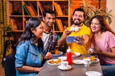 Kafede komik videolar izliyorlar, Hintli Asyalı genç üniversite arkadaşları ya da üniversite öğrencileri samosa yerken yüksek sesle gülüyorlar, sıcak çay yudumluyorlar, kapalı alanda komedi kliplerinin keyfini çıkarıyorlar.