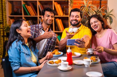 Kafede komik videolar izliyorlar, Hintli Asyalı genç üniversite arkadaşları ya da üniversite öğrencileri samosa yerken yüksek sesle gülüyorlar, sıcak çay yudumluyorlar, kapalı alanda komedi kliplerinin keyfini çıkarıyorlar.