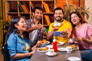 Kafede komik videolar izliyorlar, Hintli Asyalı genç üniversite arkadaşları ya da üniversite öğrencileri samosa yerken yüksek sesle gülüyorlar, sıcak çay yudumluyorlar, kapalı alanda komedi kliplerinin keyfini çıkarıyorlar.