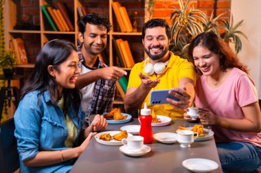 Kafede komik videolar izliyorlar, Hintli Asyalı genç üniversite arkadaşları ya da üniversite öğrencileri samosa yerken yüksek sesle gülüyorlar, sıcak çay yudumluyorlar, kapalı alanda komedi kliplerinin keyfini çıkarıyorlar.