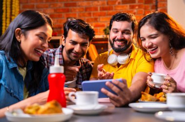 Kafede komik videolar izliyorlar, Hintli Asyalı genç üniversite arkadaşları ya da üniversite öğrencileri samosa yerken yüksek sesle gülüyorlar, sıcak çay yudumluyorlar, kapalı alanda komedi kliplerinin keyfini çıkarıyorlar.