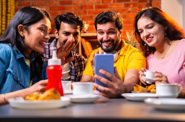 Samosa ve chai içerisindeyken arkadaşlarıyla video görüşmelerine katılan, Kafe 'de gülümseyen, akıllı telefonlarla sohbet eden, kapalı alanda neşeli anları paylaşan, arkadaşlarıyla iletişim kuran Hintli Asyalı üniversite arkadaşları.