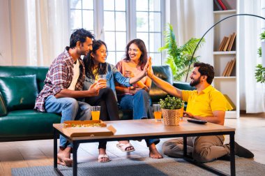 Hintli arkadaşlar kameraya gülümserken rahat bir koltukta oturup pizza yiyorlar, birlikte gündelik zaman geçiriyorlar, kaynaşıyorlar, gülüyorlar ve modern evde dinleniyorlar.