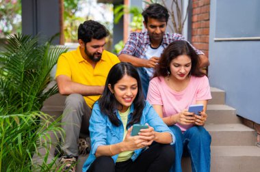 Üniversite öğrencileri açık havada akıllı telefon kullanmakla meşguller, Hindistan 'daki Asya Üniversitesi' nden sınıf arkadaşları merdivenlerde oturuyor veya kampüste duvara yaslanırken cep telefonuyla sosyal medyada kayıyor, mesajlaşıyor ya da sörf yapıyor.