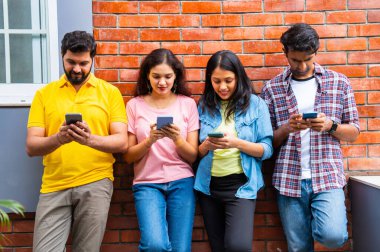 Üniversite öğrencileri açık havada akıllı telefon kullanmakla meşguller, Hindistan 'daki Asya Üniversitesi' nden sınıf arkadaşları merdivenlerde oturuyor veya kampüste duvara yaslanırken cep telefonuyla sosyal medyada kayıyor, mesajlaşıyor ya da sörf yapıyor.