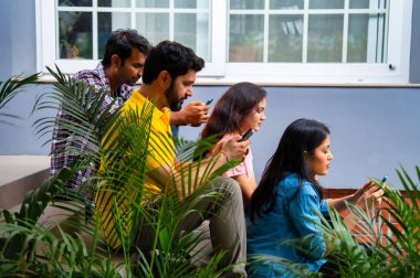 Üniversite öğrencileri açık havada akıllı telefon kullanmakla meşguller, Hindistan 'daki Asya Üniversitesi' nden sınıf arkadaşları merdivenlerde oturuyor veya kampüste duvara yaslanırken cep telefonuyla sosyal medyada kayıyor, mesajlaşıyor ya da sörf yapıyor.