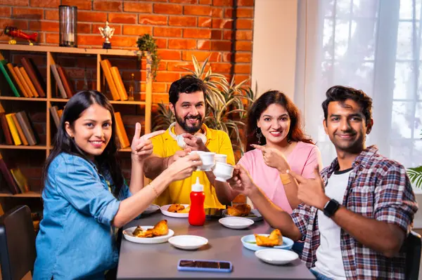 Hintli arkadaşlar sıcak çayın keyfini çıkarıyorlar, Asyalı genç üniversite öğrencileri kapalı bir lokantada oturmuş çay içiyor ya da cam bardaklardan kahve içiyor, arkadaşça sohbetler sırasında gülümsüyor ve kaynaşıyorlar.