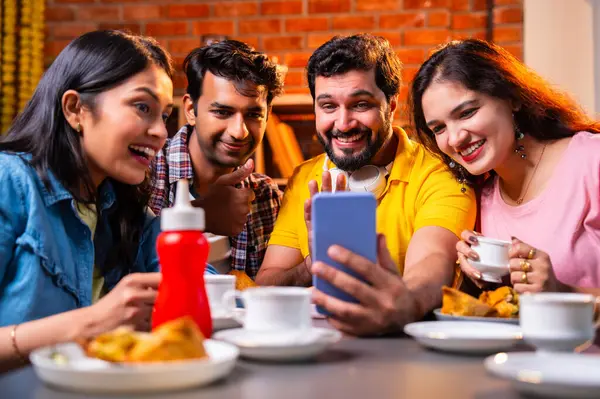 Samosa ve chai içerisindeyken arkadaşlarıyla video görüşmelerine katılan, Kafe 'de gülümseyen, akıllı telefonlarla sohbet eden, kapalı alanda neşeli anları paylaşan, arkadaşlarıyla iletişim kuran Hintli Asyalı üniversite arkadaşları.