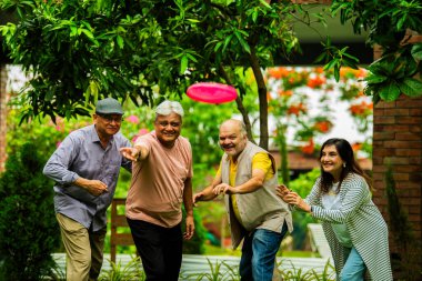 Kıdemli arkadaşlar açık havada frizbi oynamaktan zevk alıyorlar, Hintli Asyalı yaşlı grup bahçede uçan diskle oynuyorlar, birlikte gülüyorlar ve gülüyorlar yemyeşil doğa ortamında bir araya gelişimizi kutluyorlar.