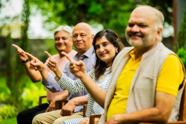 Hintli yaşlılar dışarıyı gösteriyor, Asyalı yaşlı arkadaşlar yemyeşil bahçe arka planına karşı sıralanmış, gülümsüyor ve kameraya bakarak olumlu ifadeler sergiliyorlar.