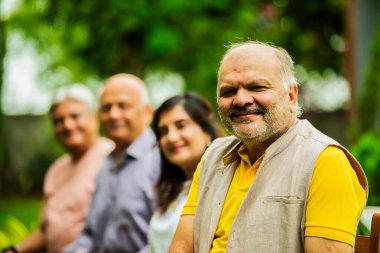 Hintli yaşlılar dışarıyı gösteriyor, Asyalı yaşlı arkadaşlar yemyeşil bahçe arka planına karşı sıralanmış, gülümsüyor ve kameraya bakarak olumlu ifadeler sergiliyorlar.