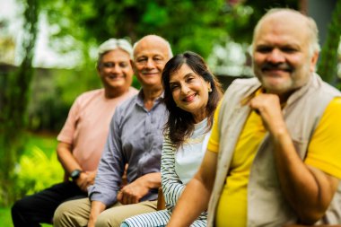 Hintli yaşlılar dışarıyı gösteriyor, Asyalı yaşlı arkadaşlar yemyeşil bahçe arka planına karşı sıralanmış, gülümsüyor ve kameraya bakarak olumlu ifadeler sergiliyorlar.