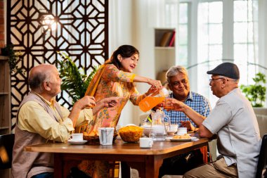 Son sınıflar birlikte yemek yiyor, Hintli Asyalı yaşlı arkadaşlar evde bir araya geliyor, yemek yiyor, atıştırmalık, soğuk içecek, çay ya da kahve servisi yapıyor, modern yemek masasında oturmuş, eğleniyorlar.
