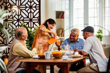 Son sınıflar birlikte yemek yiyor, Hintli Asyalı yaşlı arkadaşlar evde bir araya geliyor, yemek yiyor, atıştırmalık, soğuk içecek, çay ya da kahve servisi yapıyor, modern yemek masasında oturmuş, eğleniyorlar.