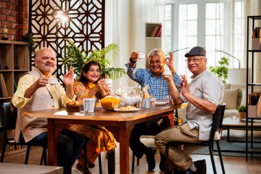 Son sınıflar birlikte yemek yiyor, Hintli Asyalı yaşlı arkadaşlar evde bir araya geliyor, yemek yiyor, atıştırmalık, soğuk içecek, çay ya da kahve servisi yapıyor, modern yemek masasında oturmuş, eğleniyorlar.