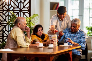 Hint kıdemli yetişkinler, Hint evinde yemek masasında oturmuş, gülüyor, eğlenceli anları kutluyor, kaynaşıyor, arkadaşça bir araya gelip eğleniyorlar.