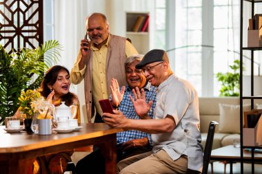 Yemek masasında son sınıfların videosu, Hintli Asyalı yaşlıların evde buluşması, akıllı telefon kullanarak grup toplantısına katılması, modern kapalı yemek düzeninde çay, atıştırma ve arkadaşça sohbetler.