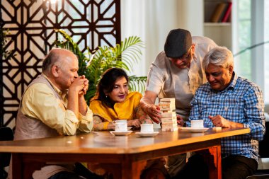 Hint kıdemli yetişkinler, Hint evinde yemek masasında oturmuş, gülüyor, eğlenceli anları kutluyor, kaynaşıyor, arkadaşça bir araya gelip eğleniyorlar.