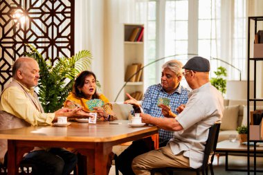 Hindistan 'daki son sınıf öğrencileri, rahat, modern bir evde yemek masasında oturmuş, neşeli bir şekilde gülüyor ve kaynaşıyorlar. Asyalı yaşlı arkadaşlar, kapalı alanda eğlenceli aktivitelerle neşeli bir buluşmayı kutluyorlar.