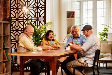 Hindistan 'daki son sınıf öğrencileri, rahat, modern bir evde yemek masasında oturmuş, neşeli bir şekilde gülüyor ve kaynaşıyorlar. Asyalı yaşlı arkadaşlar, kapalı alanda eğlenceli aktivitelerle neşeli bir buluşmayı kutluyorlar.