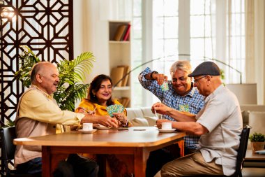 Hindistan 'daki son sınıf öğrencileri, rahat, modern bir evde yemek masasında oturmuş, neşeli bir şekilde gülüyor ve kaynaşıyorlar. Asyalı yaşlı arkadaşlar, kapalı alanda eğlenceli aktivitelerle neşeli bir buluşmayı kutluyorlar.