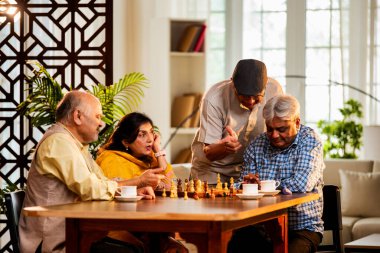 Hindistan 'daki son sınıf yetişkinler rahat bir evde yemek masasında oturmuş satranç oynarken gülümsüyor ve Shatranj maçının keyfini çıkarırken Asyalı eski dostlar kapalı alanda yeniden bir araya gelişlerini kutluyorlar.