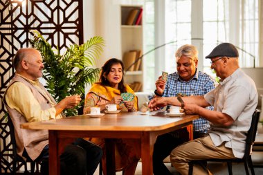 Hindistan 'daki son sınıf öğrencileri, rahat, modern bir evde yemek masasında oturmuş, neşeli bir şekilde gülüyor ve kaynaşıyorlar. Asyalı yaşlı arkadaşlar, kapalı alanda eğlenceli aktivitelerle neşeli bir buluşmayı kutluyorlar.
