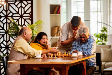 Hindistan 'daki son sınıf yetişkinler rahat bir evde yemek masasında oturmuş satranç oynarken gülümsüyor ve Shatranj maçının keyfini çıkarırken Asyalı eski dostlar kapalı alanda yeniden bir araya gelişlerini kutluyorlar.