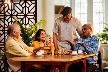 Hindistan 'daki son sınıf yetişkinler rahat bir evde yemek masasında oturmuş satranç oynarken gülümsüyor ve Shatranj maçının keyfini çıkarırken Asyalı eski dostlar kapalı alanda yeniden bir araya gelişlerini kutluyorlar.