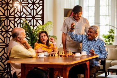 Hindistan 'daki son sınıf yetişkinler rahat bir evde yemek masasında oturmuş satranç oynarken gülümsüyor ve Shatranj maçının keyfini çıkarırken Asyalı eski dostlar kapalı alanda yeniden bir araya gelişlerini kutluyorlar.