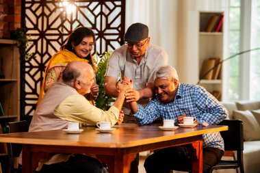 Hint son sınıf öğrencileri yemek masasında bilek güreşi ya da dostça panja oyunu oynuyorlar, ev içinde neşeyle yarışıyorlar, Asyalı yaşlı adamlar evde eğlenirken eğleniyorlar ve tezahürat yapıyorlar.