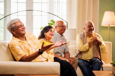 Hintli son sınıf öğrencisi rahat bir koltukta oturup televizyon izlerken gülerken Asyalı yaşlı erkekler ve kadınlar ellerinde uzaktan kumandayla televizyon izlerken televizyonda komik film ya da komedi şovu izliyorlar.