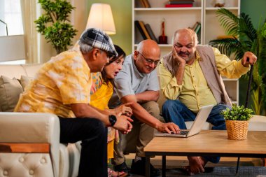 Ev içinde dizüstü bilgisayar kullanan kıdemli arkadaşlar rahat koltukta otururken Hintli Asyalı yaşlı erkekler ve kadınlar evlerinde kablosuz internet ile eğlenceli bir buluşma sırasında bilgisayarda bir şeyler planlıyorlar.